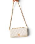 Lost Labels white quilted Chanel bag with gold chain strap held by hand against a white background