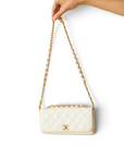 Lost Labels white quilted leather Chanel bag with gold chain strap held by a hand against a white background.