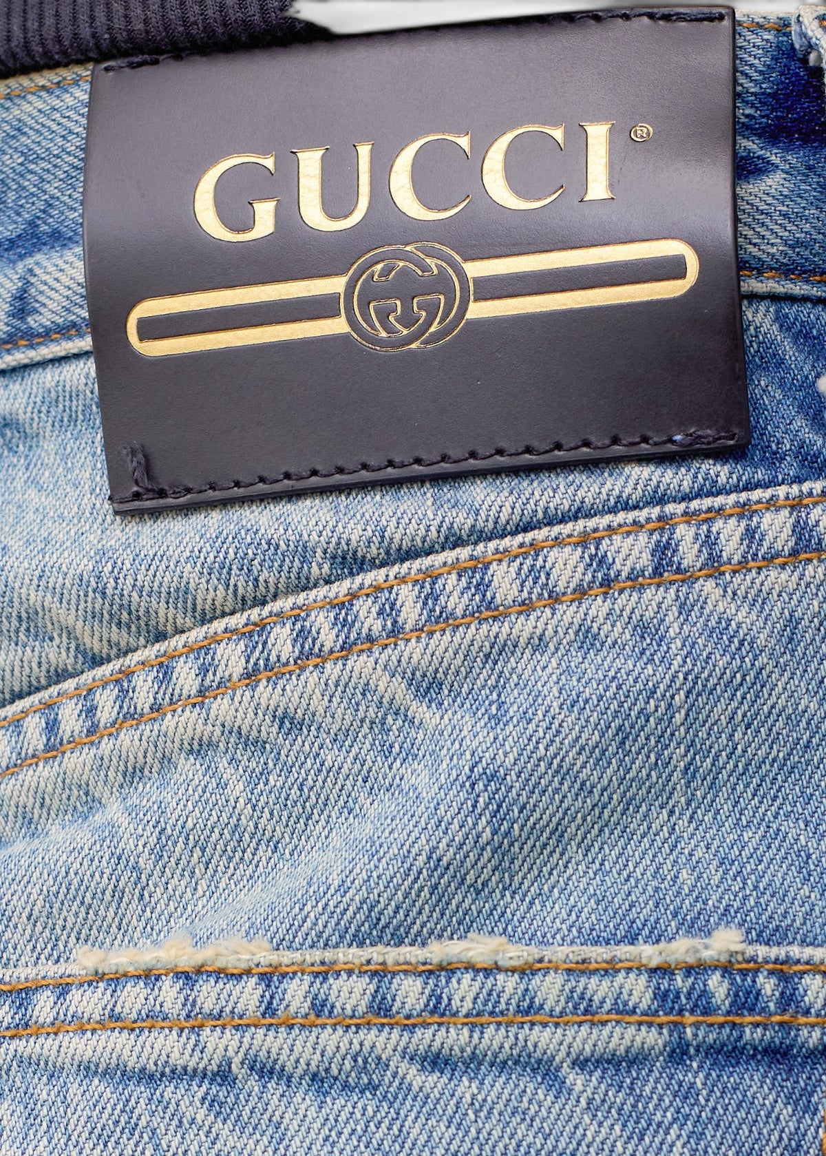 Lost Labels Gucci jeans featuring a black leather brand patch with gold logo detailing on light wash denim fabric.